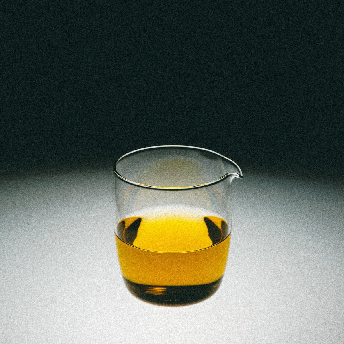 Glass tea pitcher with yellow tea on a gradient background