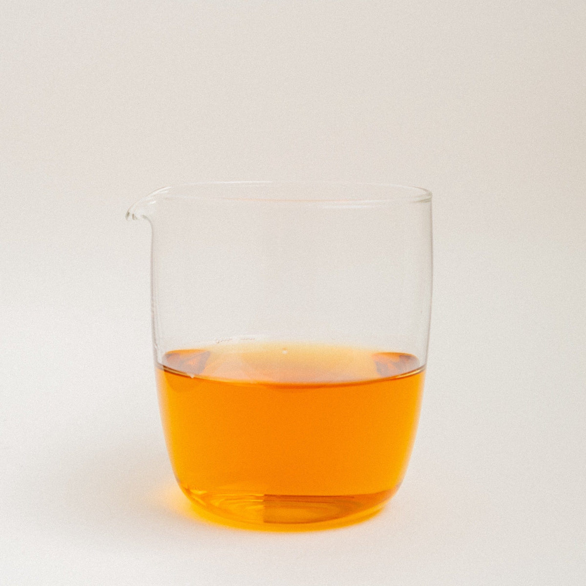 A glass tea pitcher full of amber coloured tea liquid on a white background