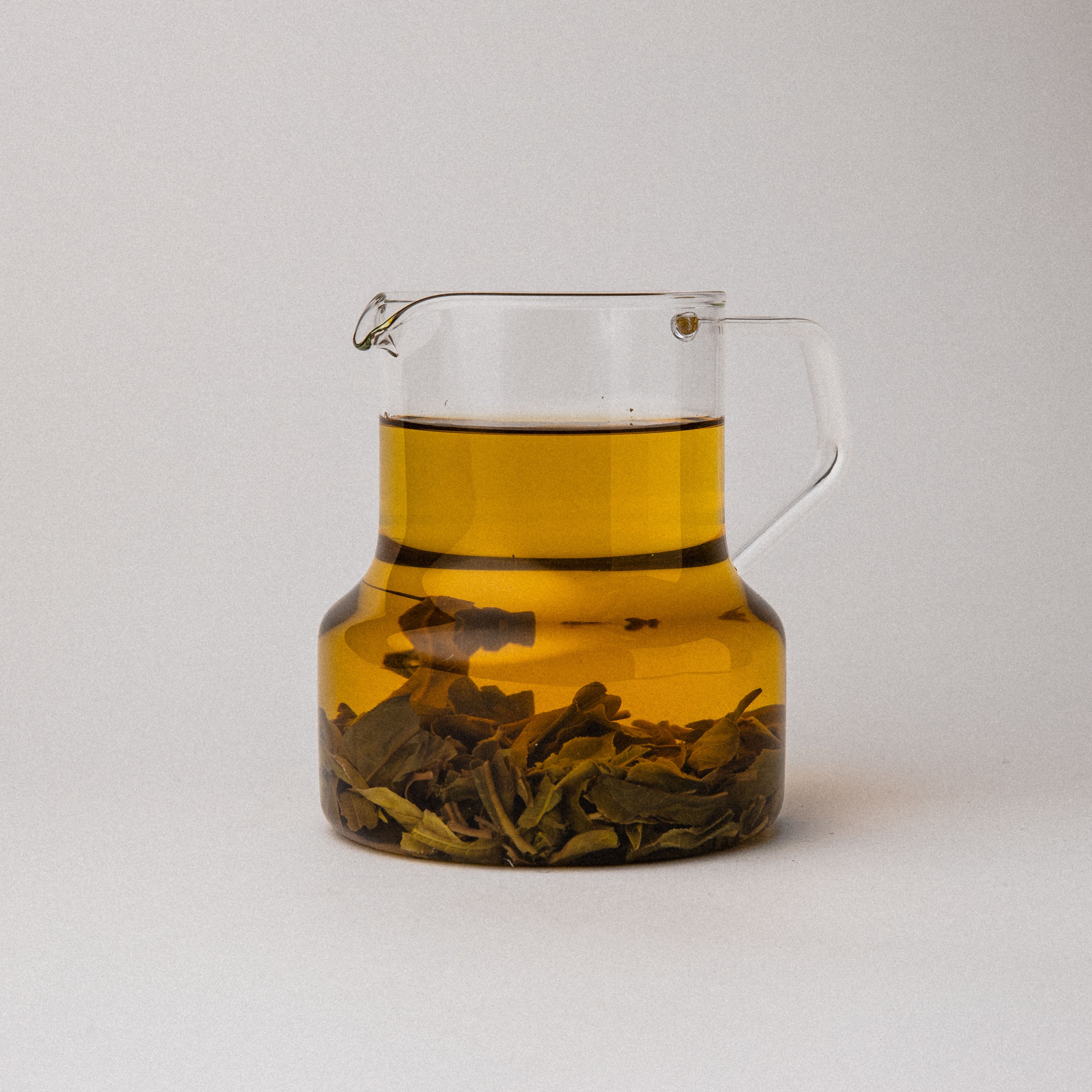 Clear glass teapot with amber liquid and tea leaves on a white background